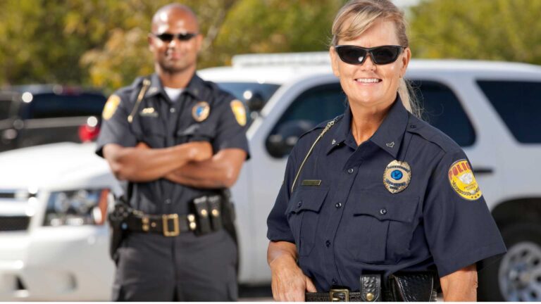 Autism and police: a male and female police officer smiling. She has her hand on her belt; he is standing with his arms crossed in the background.