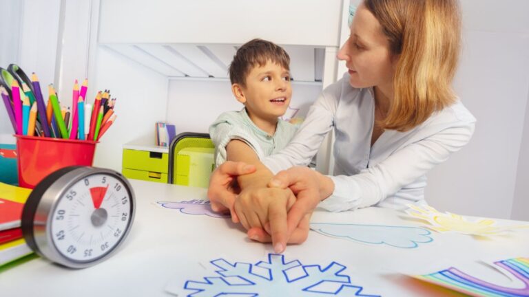 An RBT (registered behavioral technician) assists a young boy with pointing at a shape